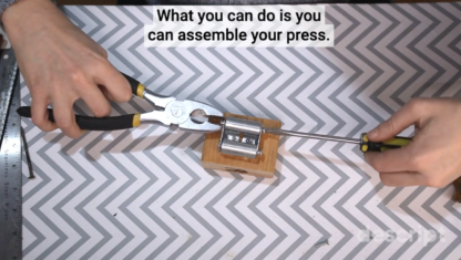 Video scene shows the DIY printing press being tightened with pliers and screwdriver